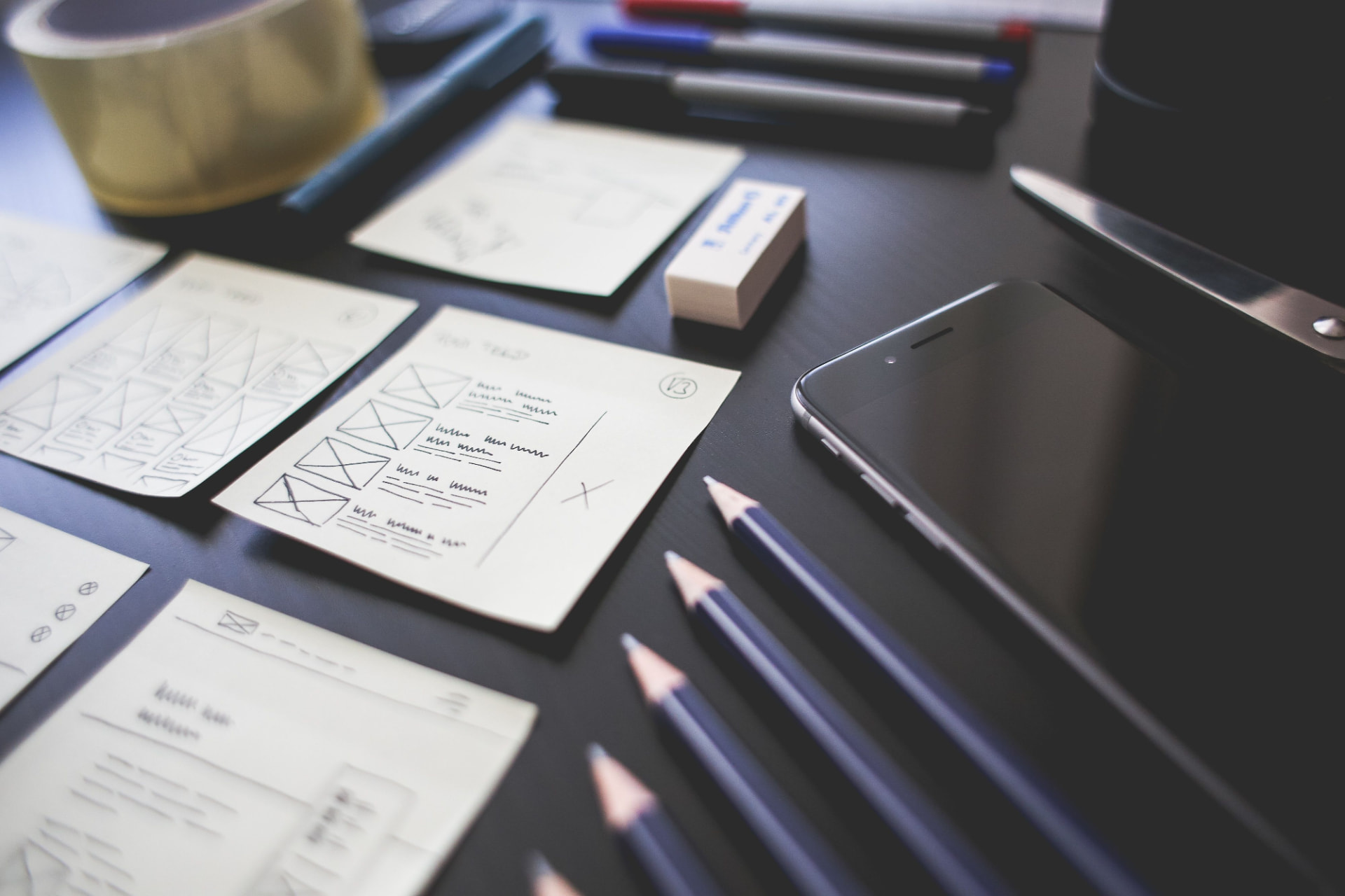 Hand-drawn workflow wireframes, pens and a phone laid out on a desk